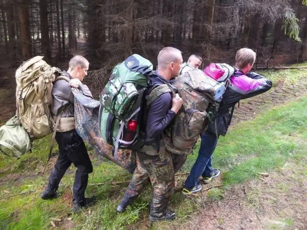 Vier Personen tragen große Rucksäcke und eine Plane durch den Wald
