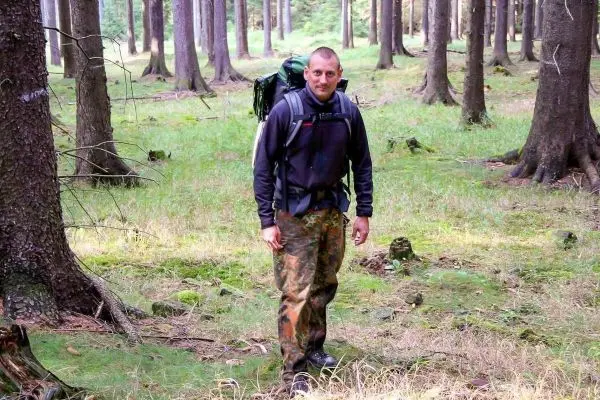 Wanderer mit Rucksack steht im Wald zwischen hohen Bäumen