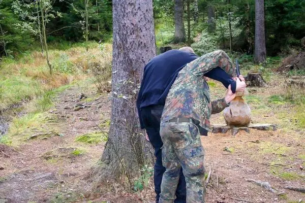 Zwei Personen heben gemeinsam einen schweren Sack in einem Waldgebiet