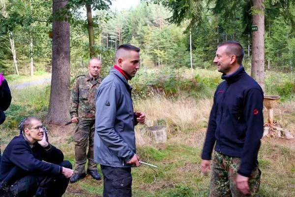 Zwei Personen im Gespräch, eine hält ein Messer, im Wald