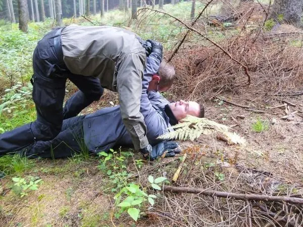 Zwei Personen im Wald, eine Person kniet über der anderen und hält sie fest