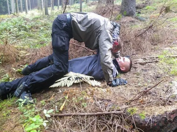 Zwei Personen im Wald, eine Person leistet Erste Hilfe auf dem Boden