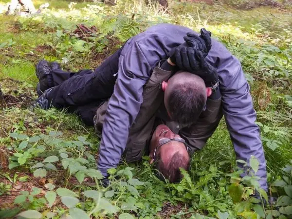 Zwei Personen liegen im Gras, eine Person hält die andere am Kopf fest