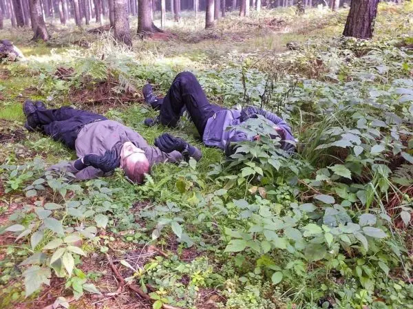 Zwei Personen liegen im Unterholz eines Waldes auf dem Boden