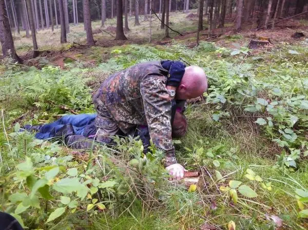 Zwei Personen liegen im Wald auf dem Boden, eine Person hält die andere fest