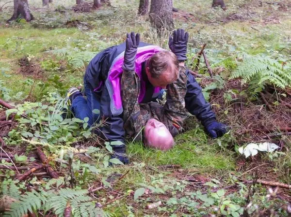 Zwei Personen liegen im Wald auf dem Boden, eine Person hält die andere in einer kontrollierenden Position