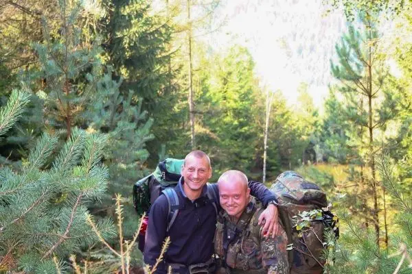 Zwei Personen mit Rucksäcken stehen im Wald zwischen Bäumen