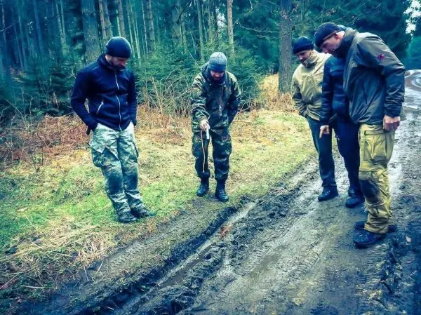 Fünf Personen betrachten eine schlammige Spur auf einem Waldweg