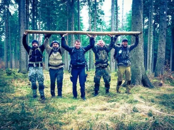 Fünf Personen tragen gemeinsam einen langen Holzstamm im Wald