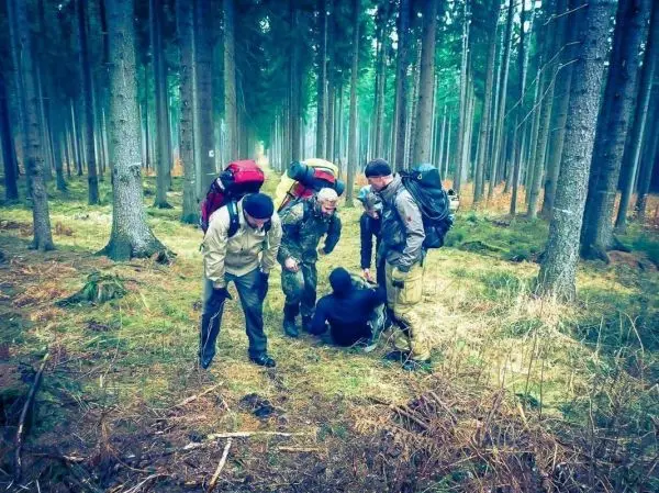 Gruppe mit Rucksäcken umkreist sitzende Person im Wald