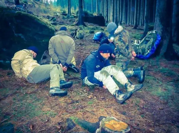 Gruppierung von Personen sitzt im Wald auf dem Boden, Rucksäcke liegen daneben