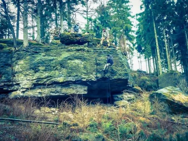 Kletterer nutzt Seil zur Besteigung eines Felsvorsprungs im Wald