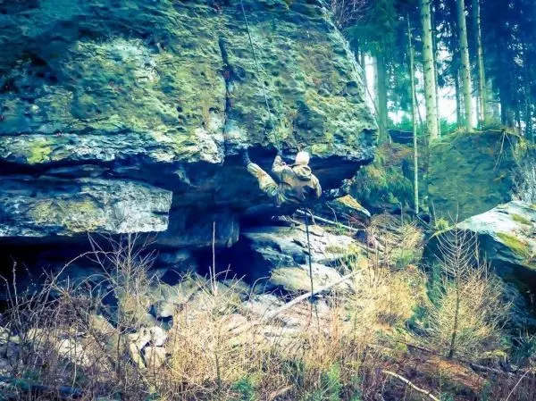 Kletterer nutzt Seil zur Überwindung eines großen Felsens im Wald