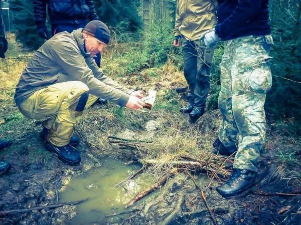 Mann hält einen Behälter über eine Wasserpfütze und zeigt darauf