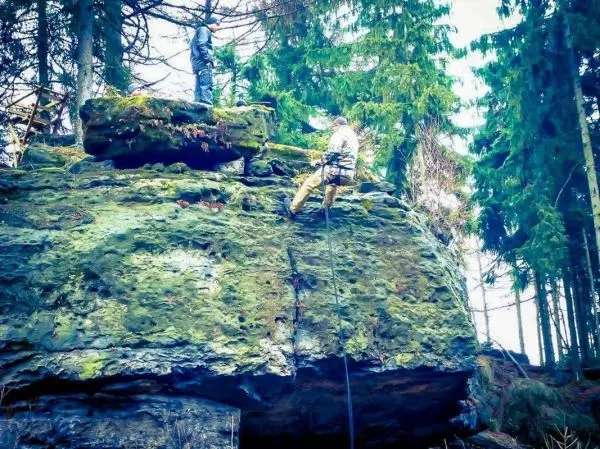 Person klettert an einer Felswand hoch, andere Person steht oben