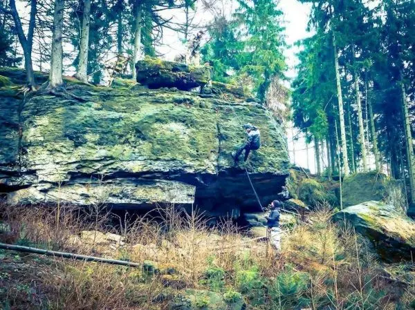 Person klettert an einer Felswand im Wald hoch
