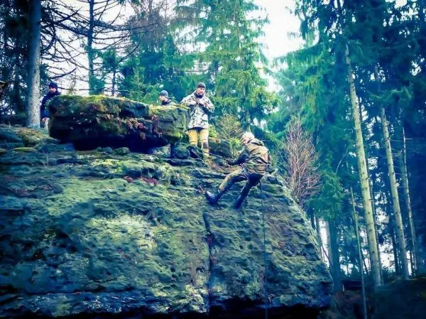 Person klettert mit Seil an einer Felswand hinunter, während andere beobachten