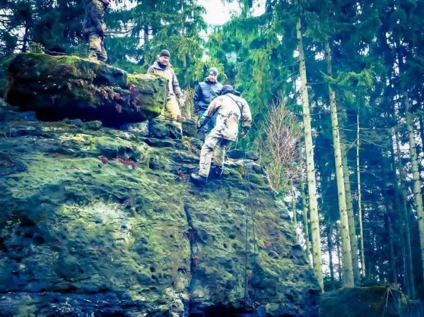 Person klettert mit Seil an einer Felswand im Wald hinunter