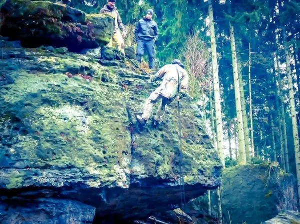 Person seilt an einer Felswand ab, während andere zuschauen