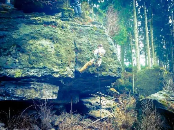 Person seilt an einer Felswand mit Sicherungsseil und Kletterausrüstung