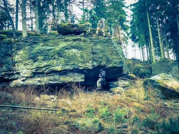 Person steht unter einem großen Felsen in einem Waldgebiet