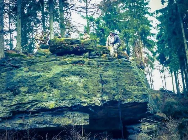 Personen stehen auf einem großen Felsen in einem Waldgebiet
