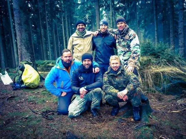 Sechs Personen posieren in einem Wald, im Hintergrund sind Bäume und Ausrüstung sichtbar