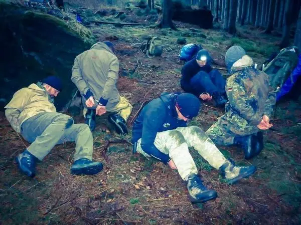 Sechs Personen sitzen mit gefesselten Händen auf dem Boden im Wald