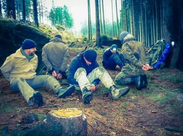 Sechs Personen sitzen mit gefesselten Händen im Wald auf dem Boden