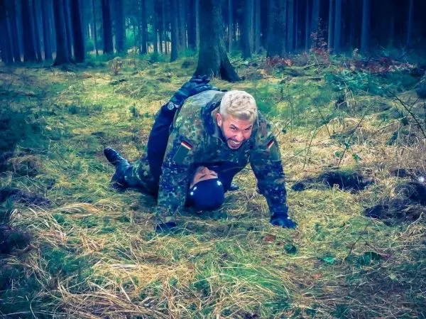 Zwei Personen im Wald, eine Person liegt auf dem Boden, die andere übt Kontrolle aus