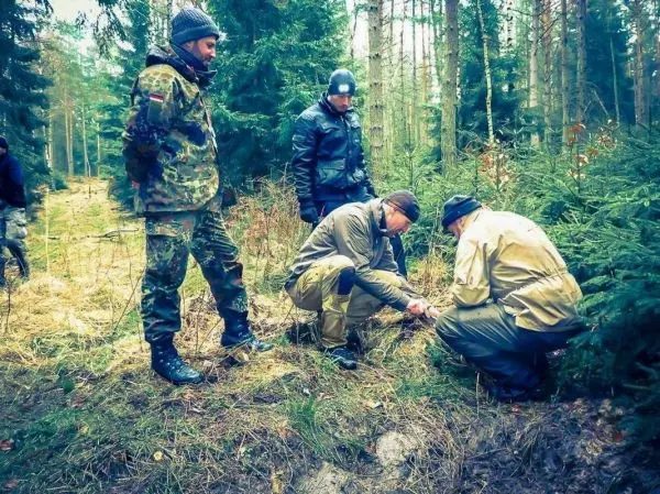 Zwei Personen knien im Wald und bereiten Zunder vor, während zwei weitere zuschauen