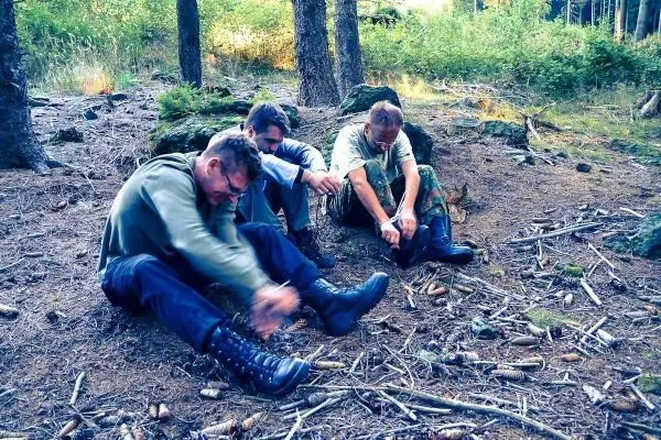 Drei Personen binden ihre Stiefel im Wald auf dem Boden