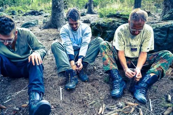 Drei Personen binden Schnüre an ihren Stiefeln im Wald