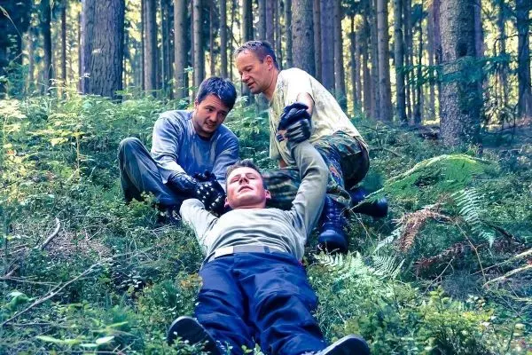 Drei Personen helfen einem Mann auf dem Boden im Wald