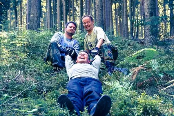 Drei Personen helfen einem Mann, der auf dem Boden liegt, in einem Waldgebiet