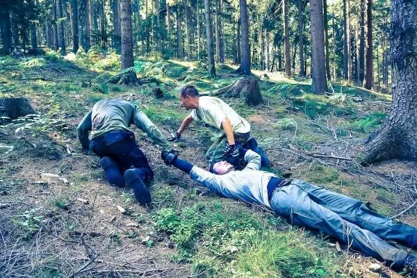 Drei Personen helfen einem Verletzten auf dem Waldboden