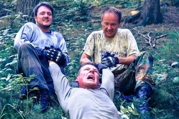 Drei Personen im Wald, eine Person wird festgehalten und schreit