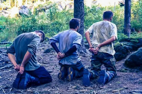 Drei Personen knien mit gefesselten Händen im Wald
