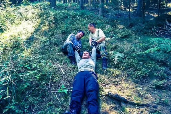 Drei Personen liegen auf einem Hang im Wald und interagieren miteinander