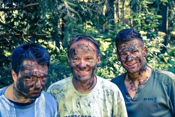 Drei Personen mit verschmutzten Gesichtern stehen im Wald