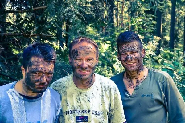 Drei Personen mit verschmutzten Gesichtern stehen im Wald