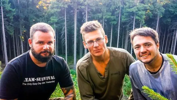 Drei Personen posieren im Wald vor einer Baumreihe