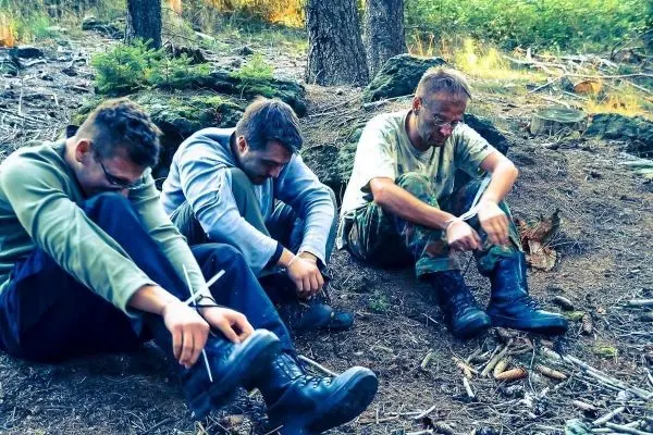 Drei Personen sitzen auf dem Boden im Wald und binden ihre Stiefel