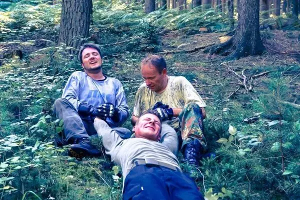 Drei Personen sitzen im Wald auf dem Boden und lachen miteinander