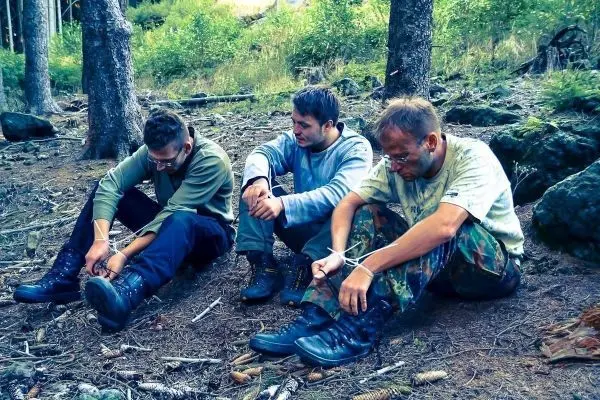 Drei Personen sitzen im Wald und binden ihre Stiefel