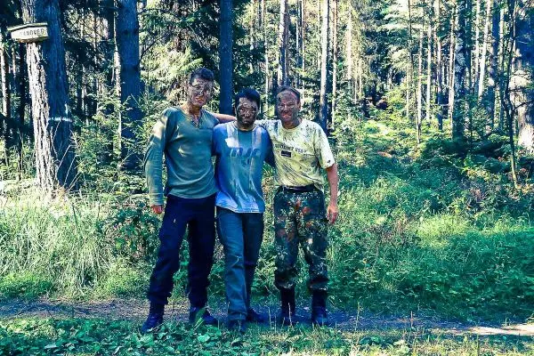 Drei Personen stehen im Wald, mit Gesichtsschminke und militärischer Kleidung