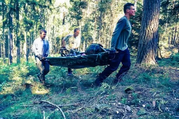 Drei Personen tragen eine improvisierte Trage durch den Wald