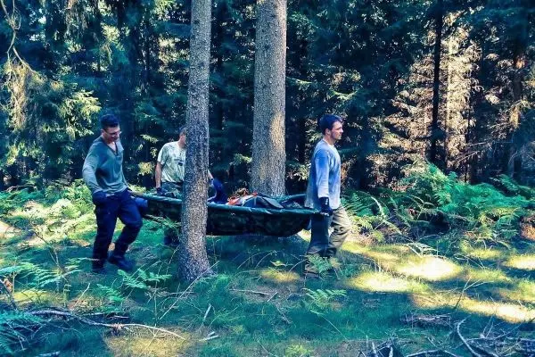 Drei Personen tragen eine improvisierte Trage durch den Wald
