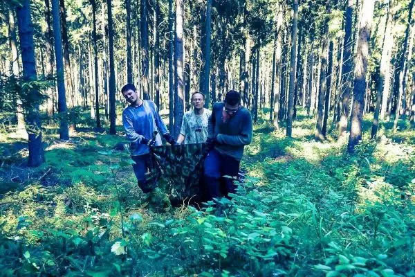 Drei Personen tragen eine improvisierte Trage durch einen Wald