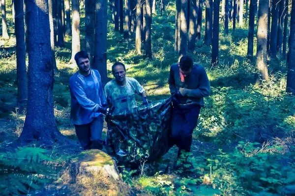 Drei Personen tragen eine improvisierte Trage durch einen Wald